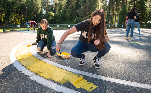 Student in the community helping paint lines on blacktop