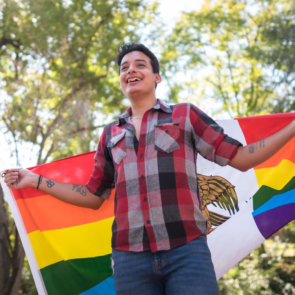 A student stands proudly wrapped in a Pride-theme Mexico flag