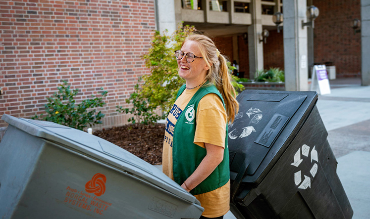 Smiling student rolls recycle bins across campus