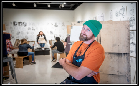 A Man in looking at the camera, in a group of people in an art studio