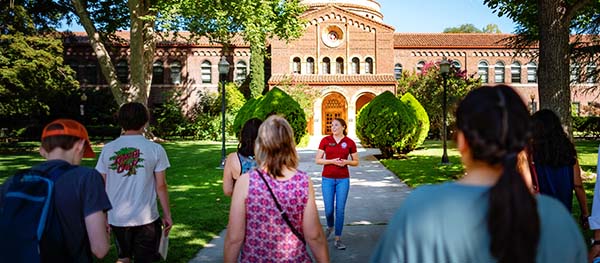 A tour guide shows families around campus on a sunny day.