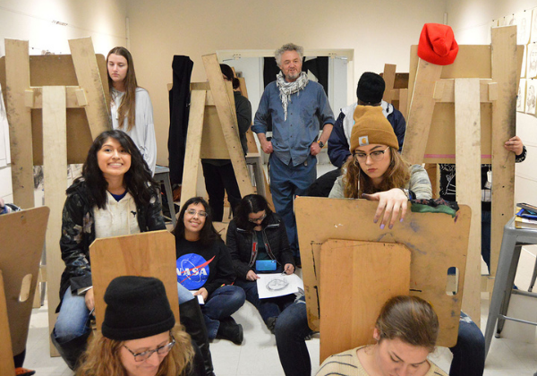 Professor J. Pouwels stands amidst students and easels drawing from a model.