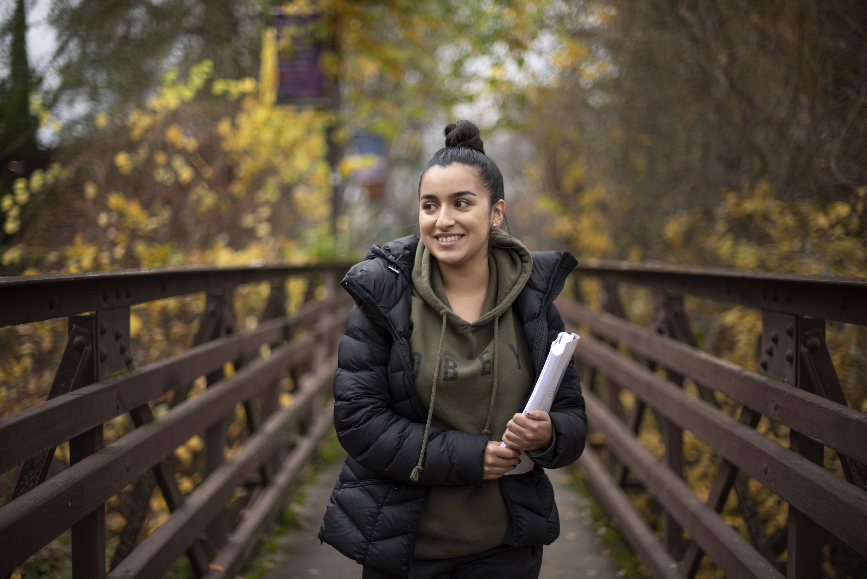 Female student walking across campus bridge and holder a notebook.