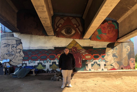 Jose Valdez in front of mural under highway overpass.