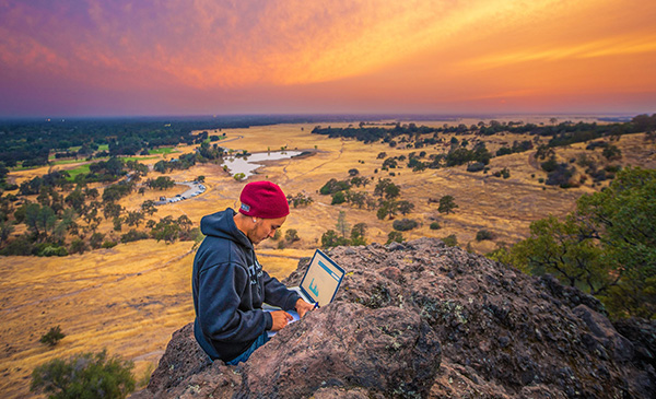 student using laptop in Upper Park during sunset with red orange sky