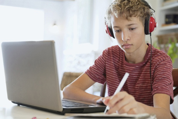 boy wearing headphones and working on laptop while taking notes