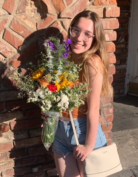Corin Hendry outside in front of a brick building holding flowers