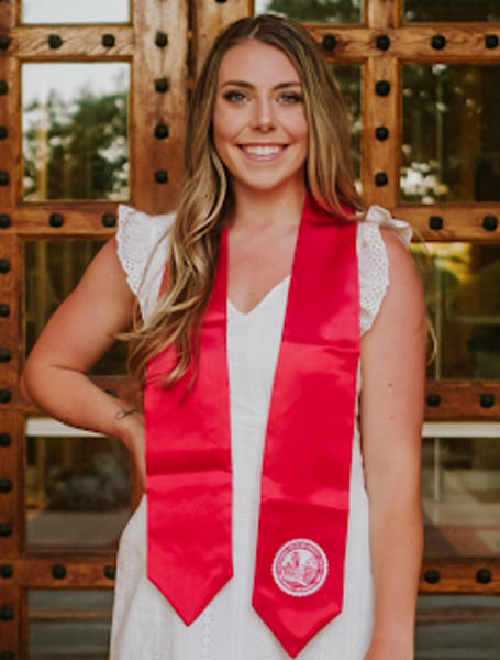 Madi standing in front of Kendall Hall wearing a white dress and sash for graduation