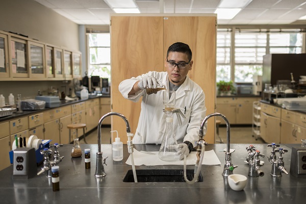 A student works in a science lab pouring liquid from one beaker to another