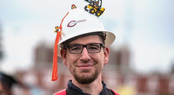 CM Graduate wearing hard hat with lego construction toys glued to the top