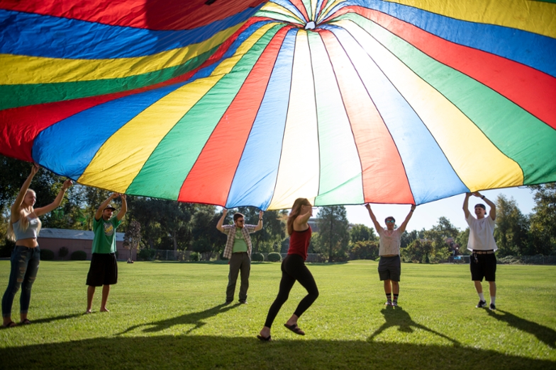 A student runs under a rainbow colored parachute