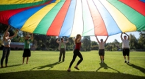 A student runs under a rainbow color parachute. 