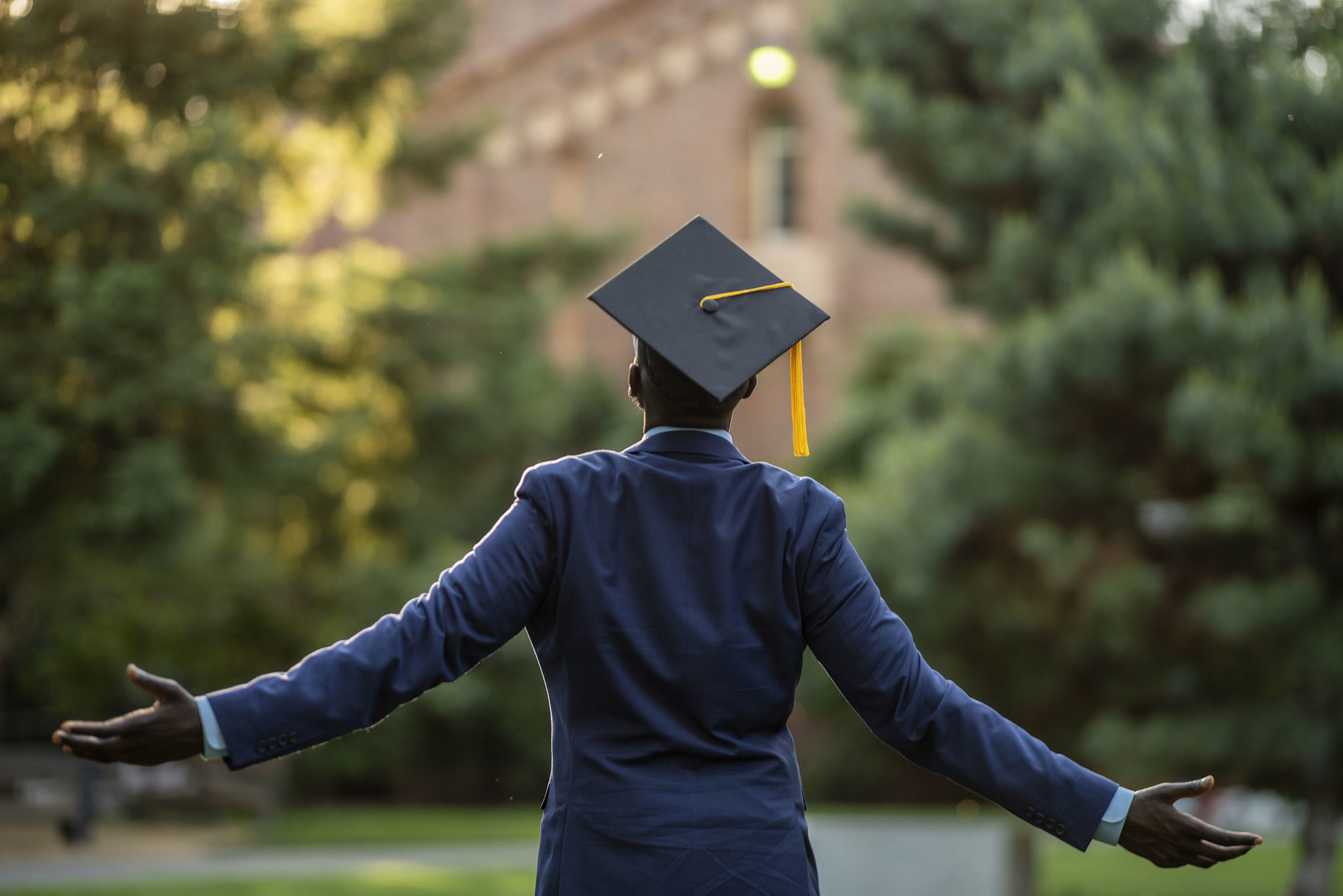 New graduate wearing mortar board hat extends his arms while facing away