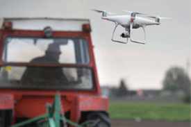 A drone flying in front of a tractor at the University Farm.