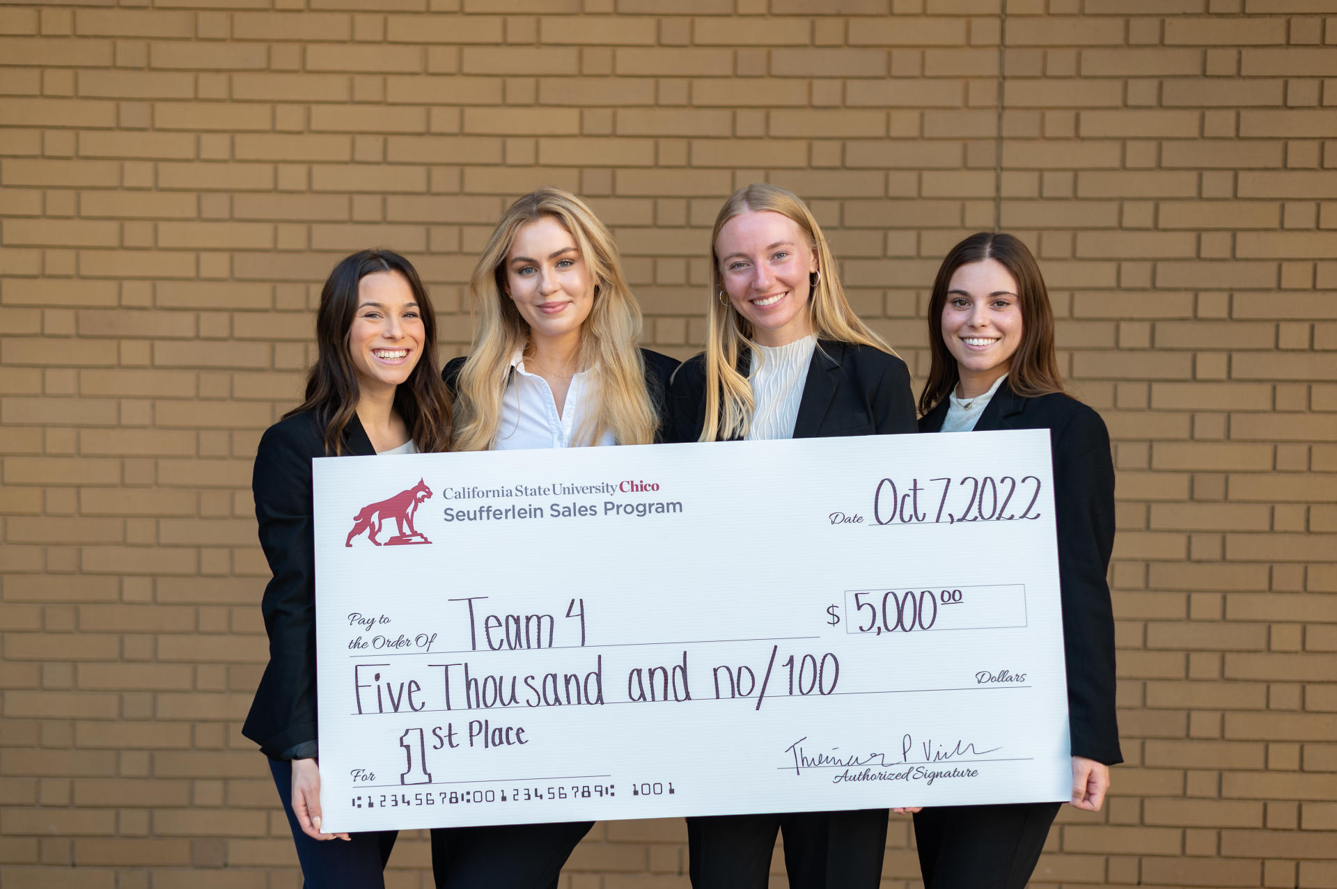 Four students holding an oversized check for $5,000