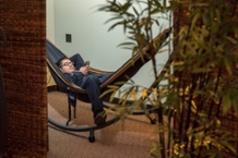A student relaxes in a hammock behind a wall partition and a bamboo plant