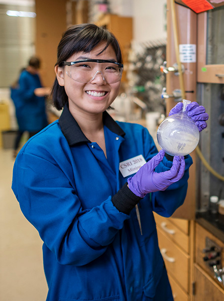 Female in lab holding beaker smiling