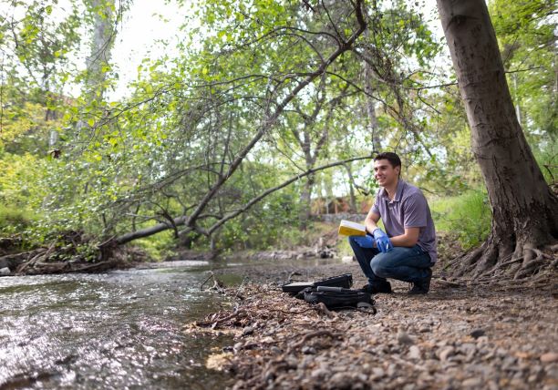 Environmental Science student, Zach Burr, recording data in a notebook along the creek