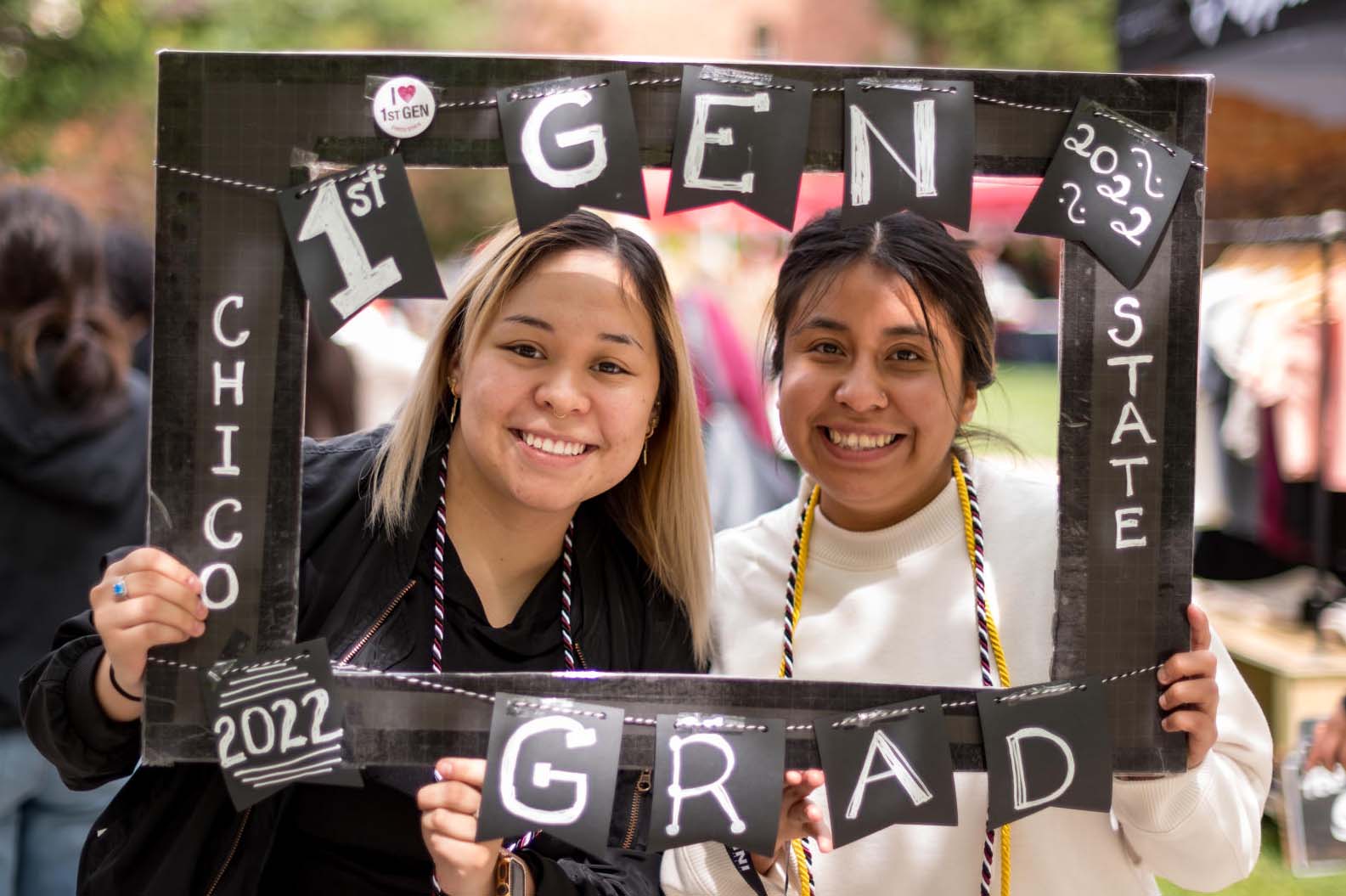 Two students hold up a cardboard frame that reads "First Gen Chico State Grad"