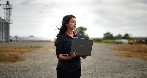 Person holding a laptop in a rural, farm-like setting
