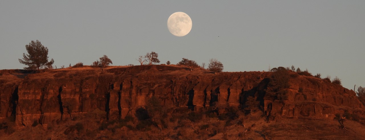 a full moon rises above the butte creek cliffs