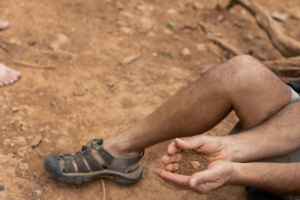 A man sits on the ground with a handful of soil.