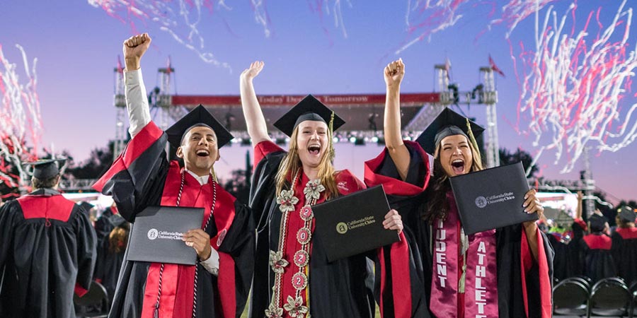 Three graduates celebrate at Commencement as confetti bursts from the stage
