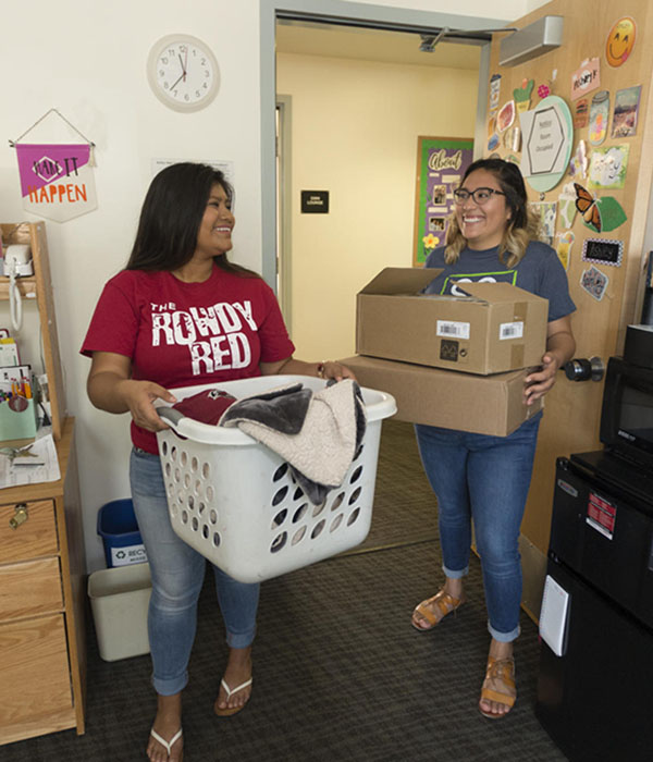 Two students carry boxes as they move into a dorm room