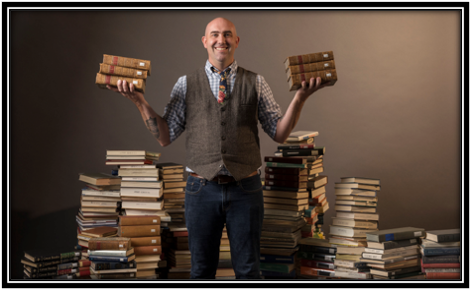 Professor Corey Sparks holding books and standing amongst books.