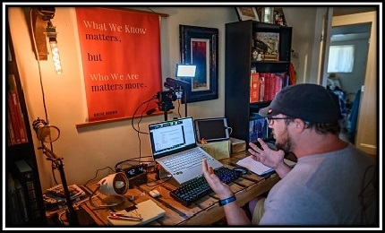 A man sitting at his laptop, recording a podcast