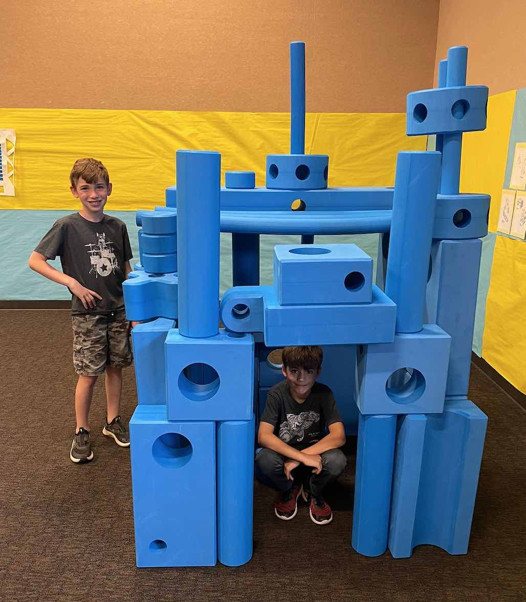 two young boys standing by a castle built of blue blocks