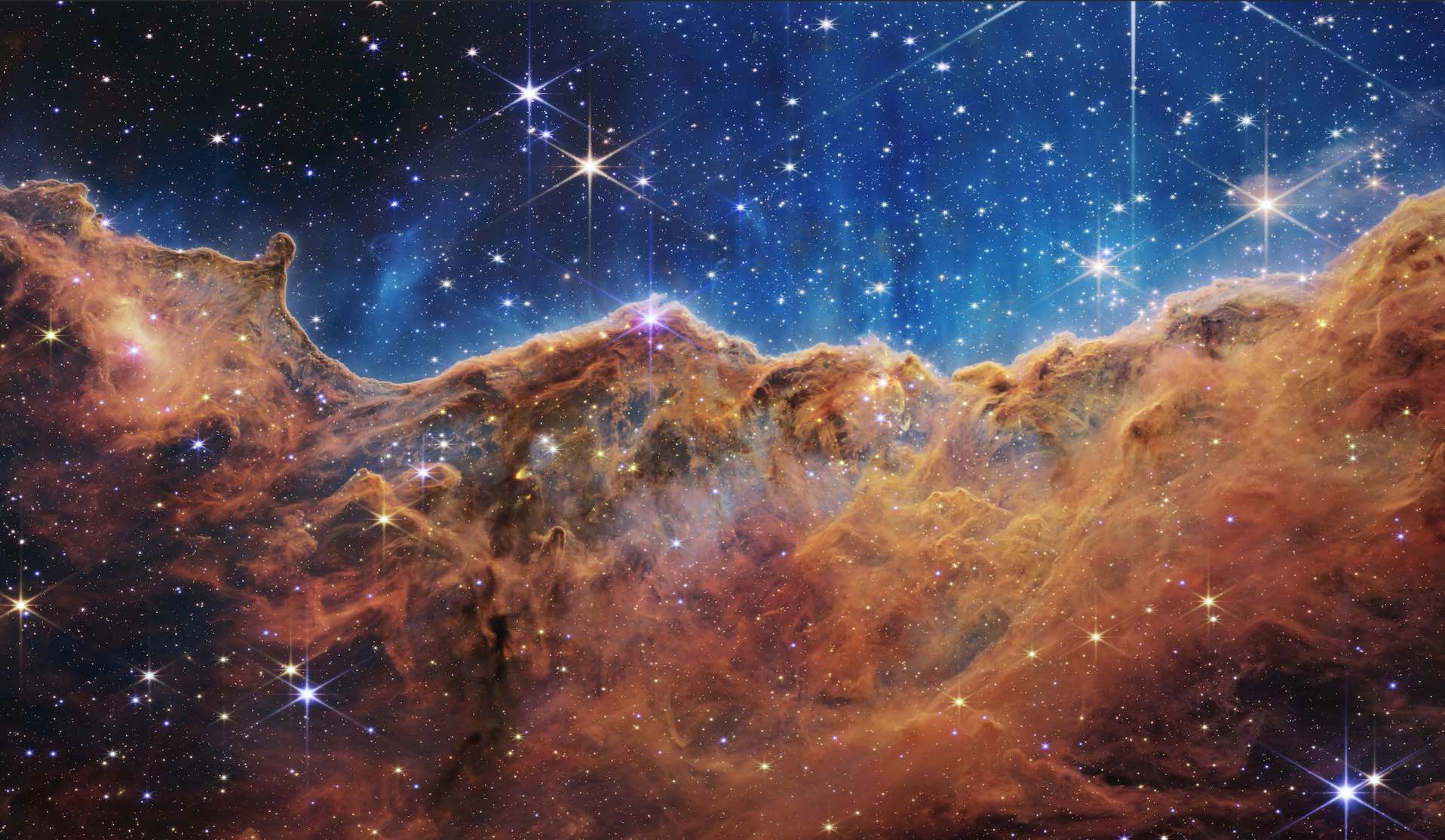 A large wall of orange star material in space, the sky above is blue against the black sky