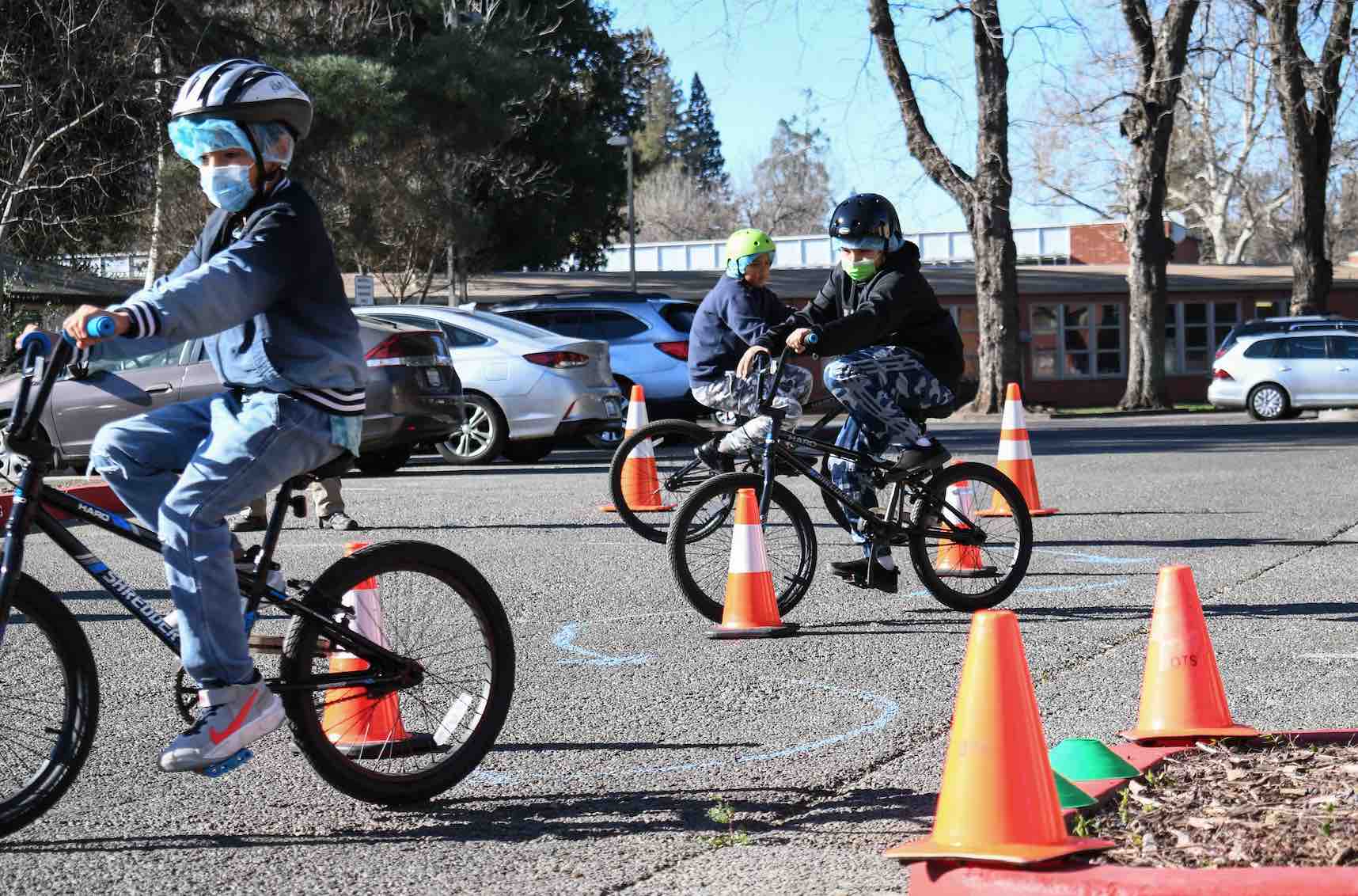 three boys ride bikes around traffic cones
