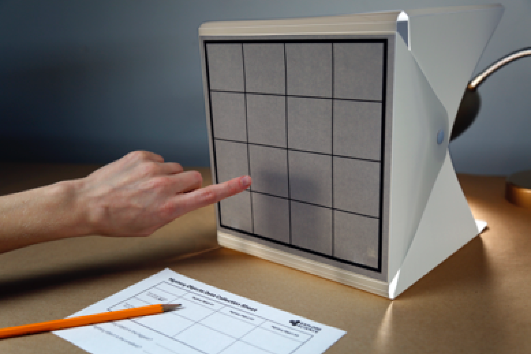A finger pointing at a light box with a grid of sixteen squares.