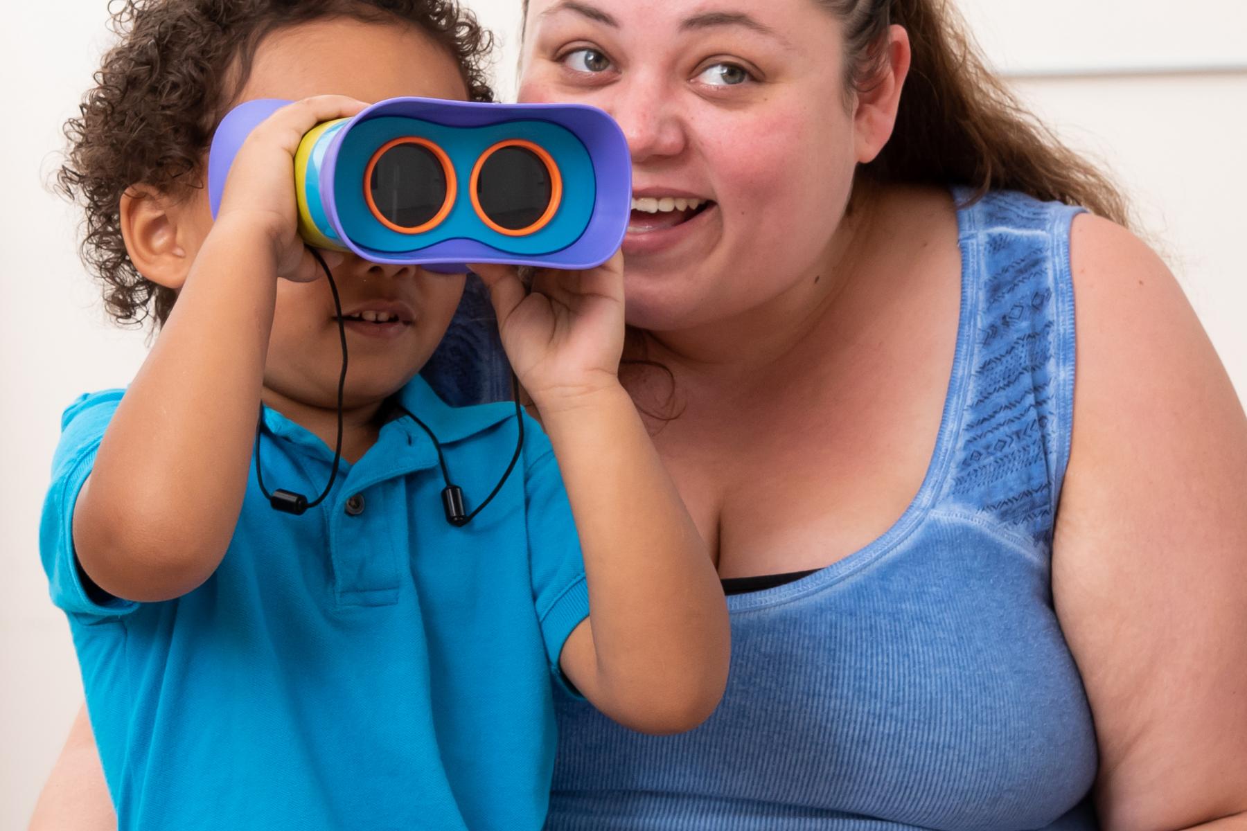 A young child holds binoculars to his face. 