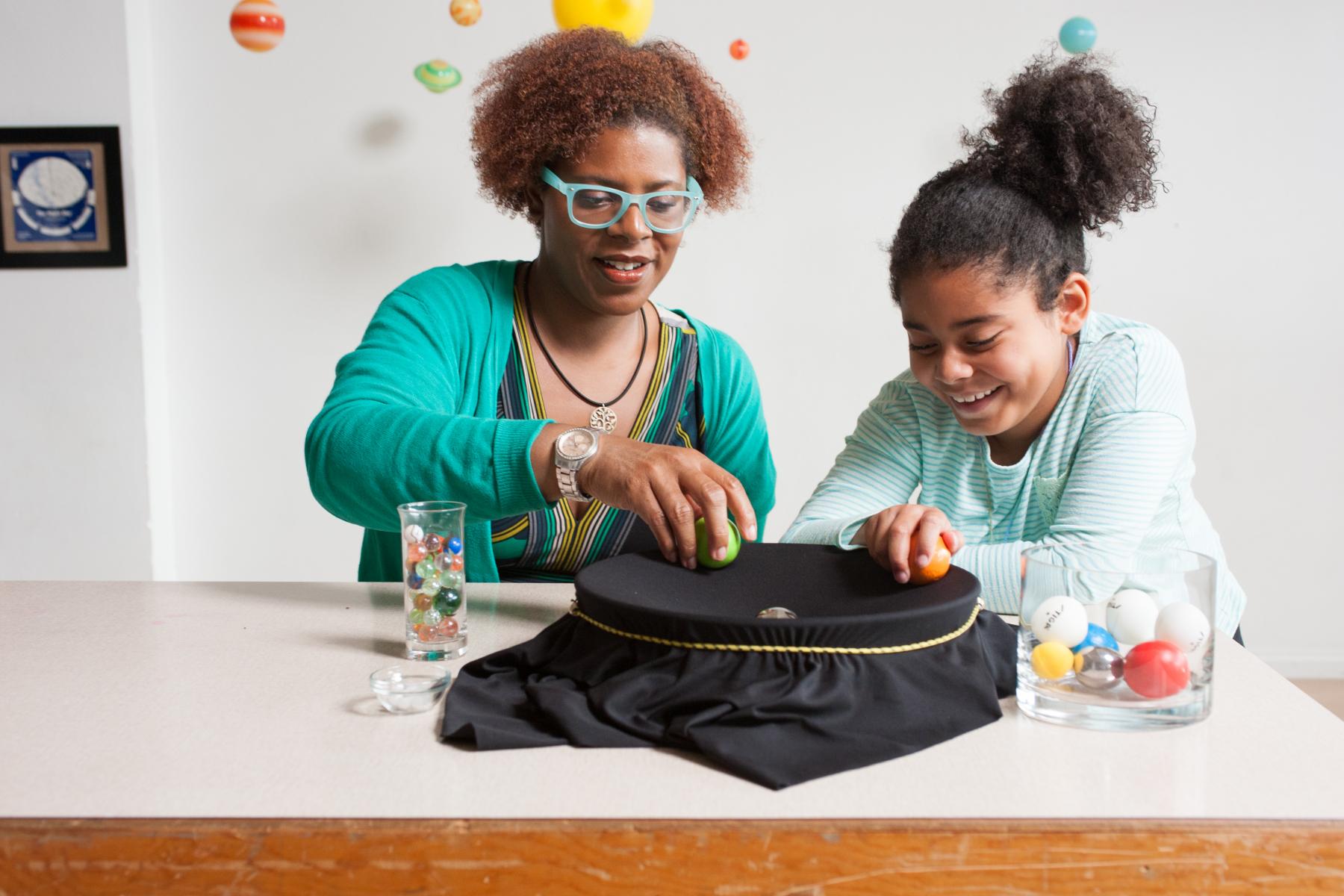 Adult and child sit at a table and work on a science project.