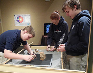Three students engage with the shake table at the When the Earth Shakes exhibit
