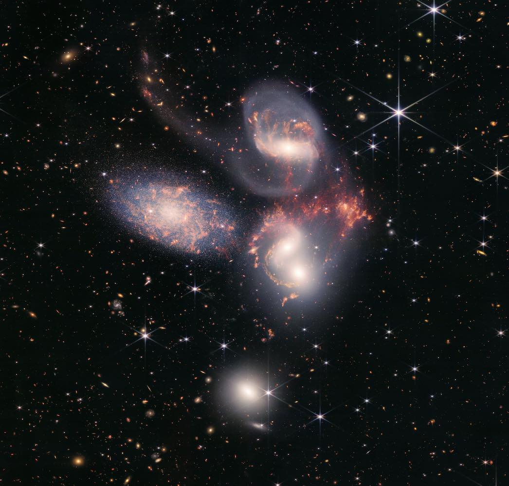 A cluster of five swirling galaxies all in white, pink, purple and orange against a black starry sky