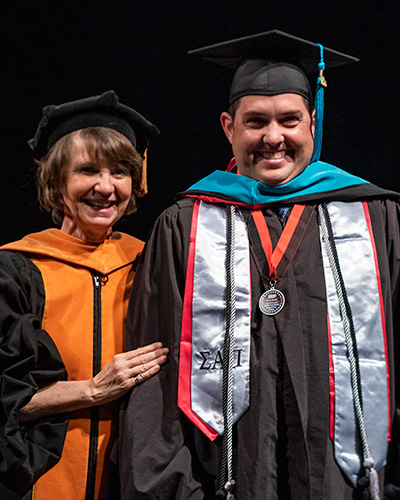 Brian Smith smiles with Provost Debra Larson during master's graduation ceremony