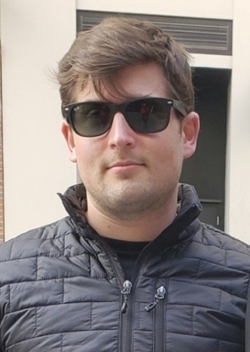 male student wearing sunglasses standing in front of a wall