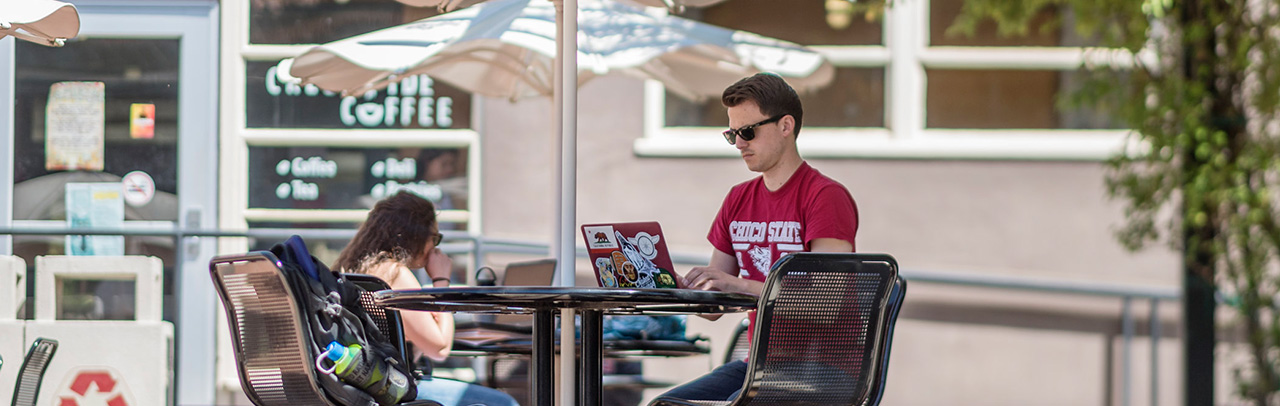Student on laptop in front of Creekside Cafe