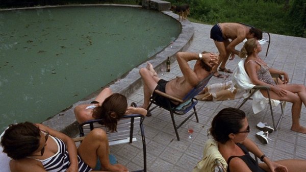 A still from the film, people are lounging by a swamp-looking pool