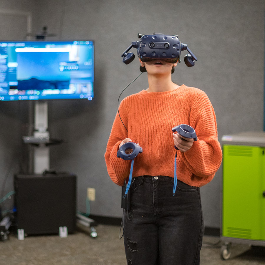 Student stands in a VR learning space with a headset and controlers