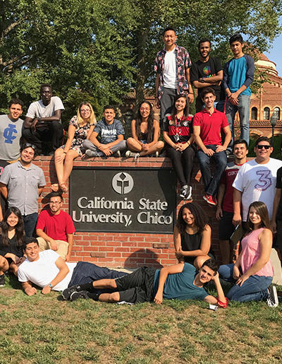 A group of students gathered around the Chico State sign on Kendall Hall's lawn.