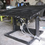 Black steel frame holding a large perforated top platform and tank with attached hoses