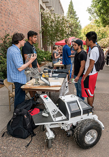 Students gather around Mechatronic Table on Campus, students showing off project