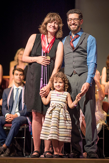 female nursing student at graduation on stage with husband and daughter