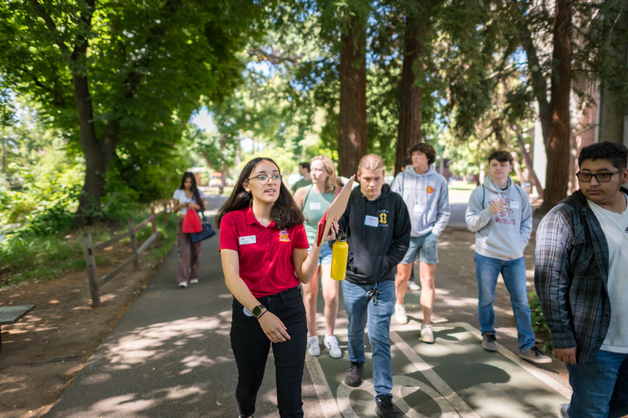 An orientation student worker directs a campus tour group along the river.