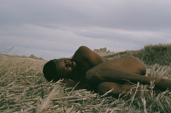 man curled up naked laying in an open field
