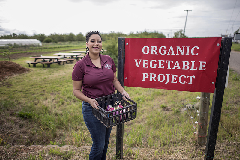 student with vegetables near the organic vegetable project sign